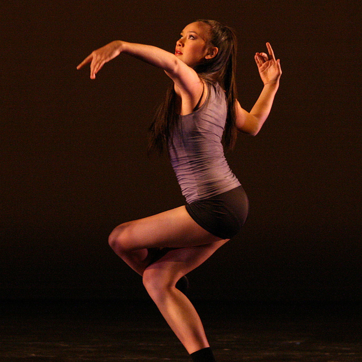 Dancer in a purple top and black shorts performing on a dark background