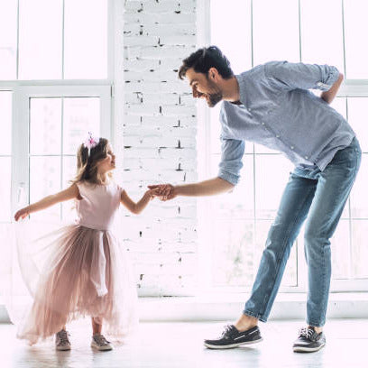 Man and young girl dancing together in a bright room with large windows.